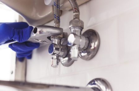 Gloved plumber tightening under-sink water supply valves with a wrench